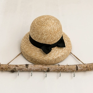 Classic dome straw sun hat with black ribbon bow hanging on a rustic wooden rack