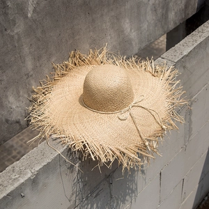 Bohemian raffia straw sun hat with frayed brim and beaded drawstring in outdoor setting