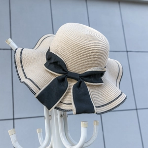 Detail of beige woven straw hat featuring a black bow and striped wavy wide brim