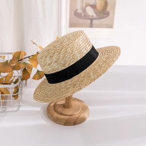 Flat top straw sun hat with black ribbon band displayed on a wooden stand