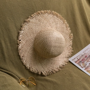 Détail d'un chapeau en paille de raphia avec bords effilochés sur fond vert olive