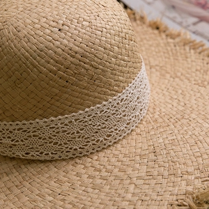 Close-up of summer raffia sun hat featuring white lace trim and natural frayed edges