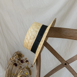 Classic straw boater hat with black grosgrain ribbon hanging on a vintage wooden chair