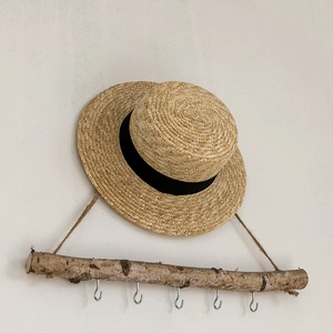 Flat top boater straw hat with black ribbon detail hanging on a rustic wooden stand