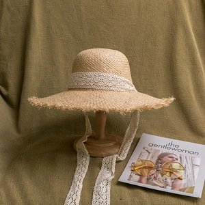 Detail of hand-woven raffia sun hat featuring crochet lace ribbon and raw fringe edge