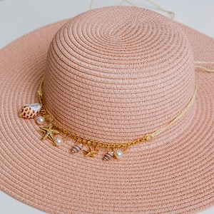 Detail of pink woven straw hat featuring gold starfish, sea shells and pearl pendants