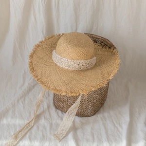 Ethnic summer straw sun hat with white lace ribbons and raw edges on a woven basket