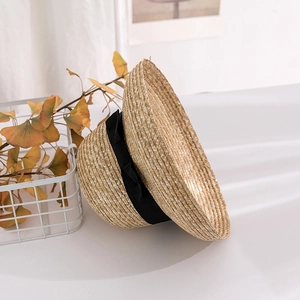 Detailed close-up of woven straw sun hat with black silk ribbon bow on white background