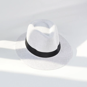 Detail of white woven straw fedora hat with black ribbon and summer sun shadow effect