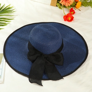 Detailed top view of a wide brim straw hat with a large black ribbon bow on white fabric