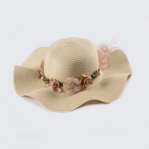 Detail of summer straw hat featuring floral wreath and elegant wavy wide brim