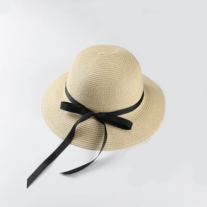 Detail of woven straw sun hat featuring a long black satin ribbon bow on a round crown