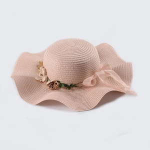 Detail of pink straw sun hat featuring floral accents and mesh ribbon on wavy brim