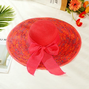 Close-up of red woven sun hat featuring large bow and colorful dots in beach style