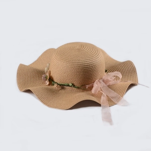 Detail of a khaki straw hat with pink flowers and a chiffon bow ribbon for beach sun protection