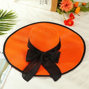 Detailed close-up of an orange wide-brim straw hat featuring a black bow and ribbon trim