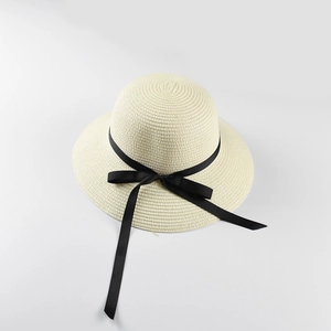 Detail of white straw sun hat featuring a classic black ribbon bow and textured weave