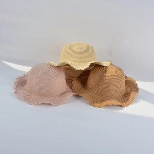 Three wavy-brim straw hats for girls in pink, beige, and tan stacked in soft natural light