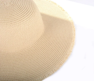 Detail of light beige straw sun hat featuring intricate woven texture and frayed fringe edges