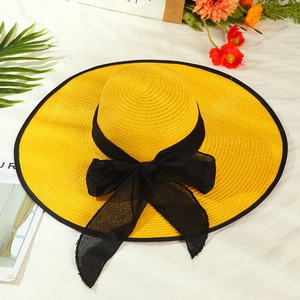 Detail of wide brim yellow straw hat featuring a black mesh bow and woven texture