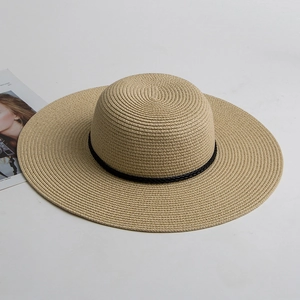 Detail of khaki straw sun hat with black woven band on a minimalist white surface
