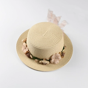 Detailed view of handmade woven straw hat featuring floral wreath and pink chiffon ribbon