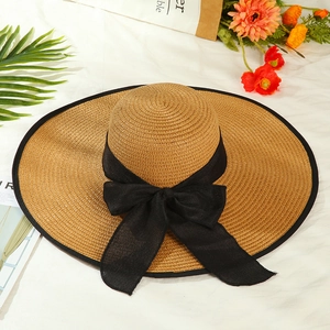 Summer wide brim straw sun hat with black bow and elegant ribbon on white fabric