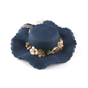 Detail of navy blue straw sun hat with wavy brim, faux silk flowers and organza ribbon