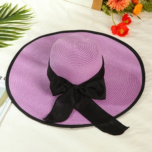 Detail of a purple wide-brim straw hat with a black bow on a white fabric backdrop