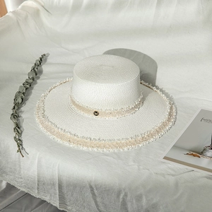 Détail d'un chapeau de paille blanc à larges bords avec franges et emblème doré M