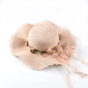 Detail of beige straw sun hat with wavy lace edges, floral vines, and long champagne ribbon