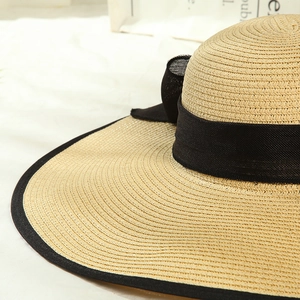 Detailed close-up of woven straw sun hat with elegant black ribbon bow and mesh trim