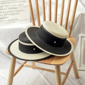 Detail of two straw boater hats with M-logo ribbon on a wooden chair for summer vacation