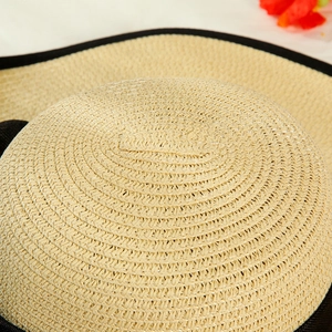 Close-up of fine spiral straw weave with black contrast edge on a beige sun hat