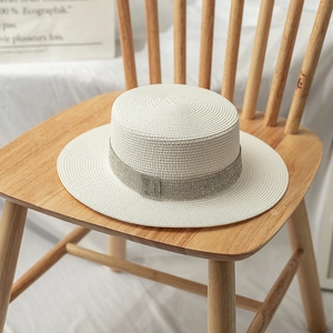 Close-up of white boater hat with sparkling rhinestone band on wooden stool