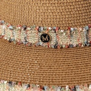 Détail d'un chapeau en paille avec fils métalliques, glands colorés et badge logo M