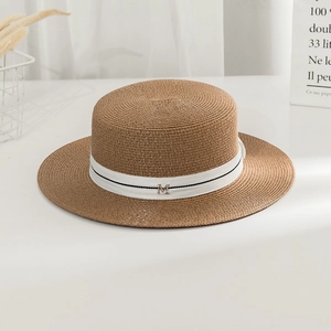 Detail of a brown straw boater hat with white ribbon and metal M letter ornament