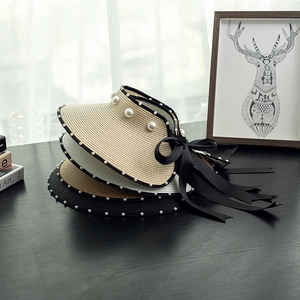 Detail of straw sun visors with pearls and black ribbon bows on a wooden table
