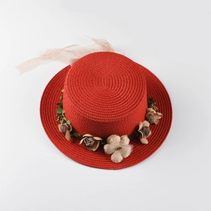Detailed close-up of red woven boater straw hat with floral decorations and ribbon