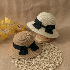 Close-up of dual-tone straw sun hats with black bow ribbons on a rustic linen background