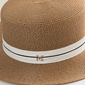 Detail of hand-woven straw hat with white ribbon and rhinestone metal M logo
