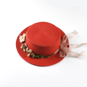 Detailed macro of a red boater straw hat featuring elegant handmade silk flowers and ribbon