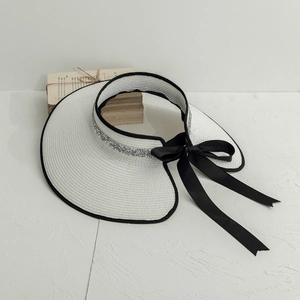 Detail of white straw sun visor with black bow ribbon and sparkling silver sequins