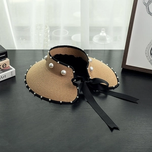 Straw sun hat with large pearls and black satin bow ribbon on a wooden background