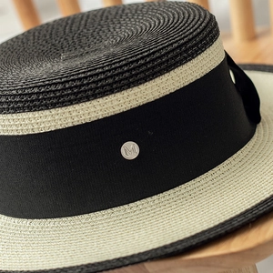 Detail of two-tone boater hat featuring black crown and silver M logo on ribbon