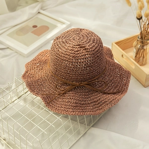 Detailed texture of brown hand-woven straw beach hat with a delicate bow and wavy brim