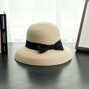 Detail of classic beige straw hat featuring wide black ribbon bow on wooden table
