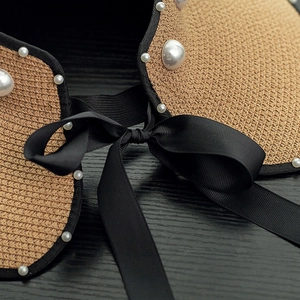 Close-up of woven straw sun hat detailing pearl accents and elegant black ribbon bow
