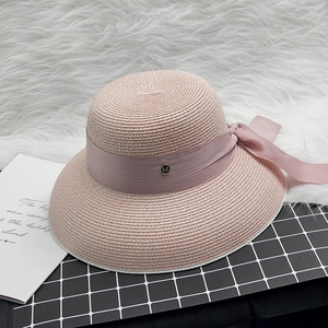 Detail eines rosa Strohhutes mit eleganter Schleife und goldener M-Metallschnalle