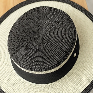 Detailed top view of a woven boater hat with a black crown and metallic logo badge